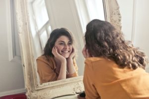 Photo of a woman smiling and looking at herself in the mirror.