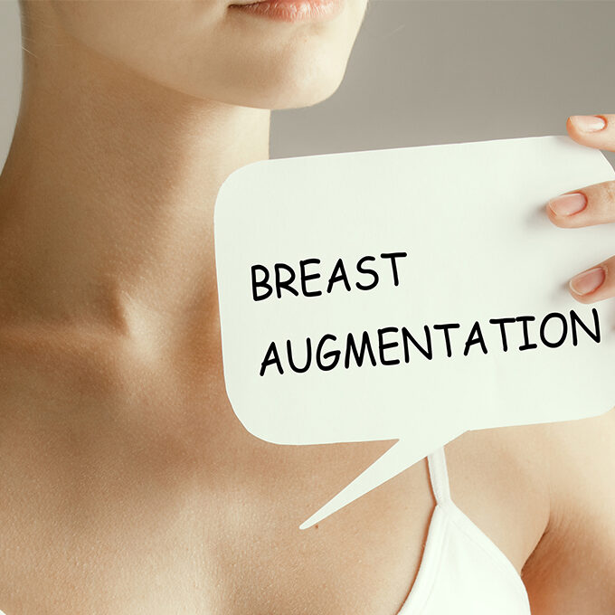 woman holding a piece of paper with breast augmentation written on it